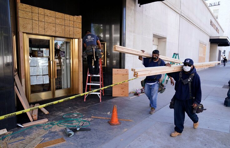 Laborers carry materials to board up windows before the upcoming election
