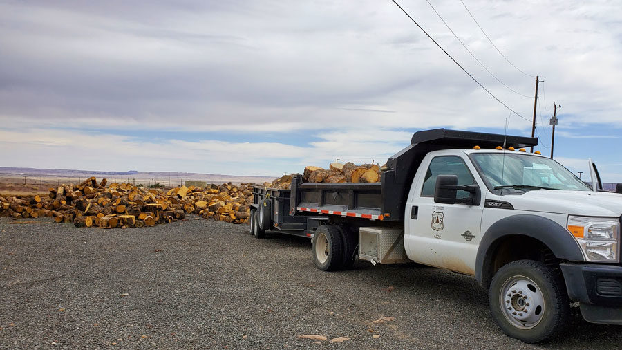 A white truck with the UDSA Forest Service shield on the door is pictured with a bed full of wood, ready for distribution.